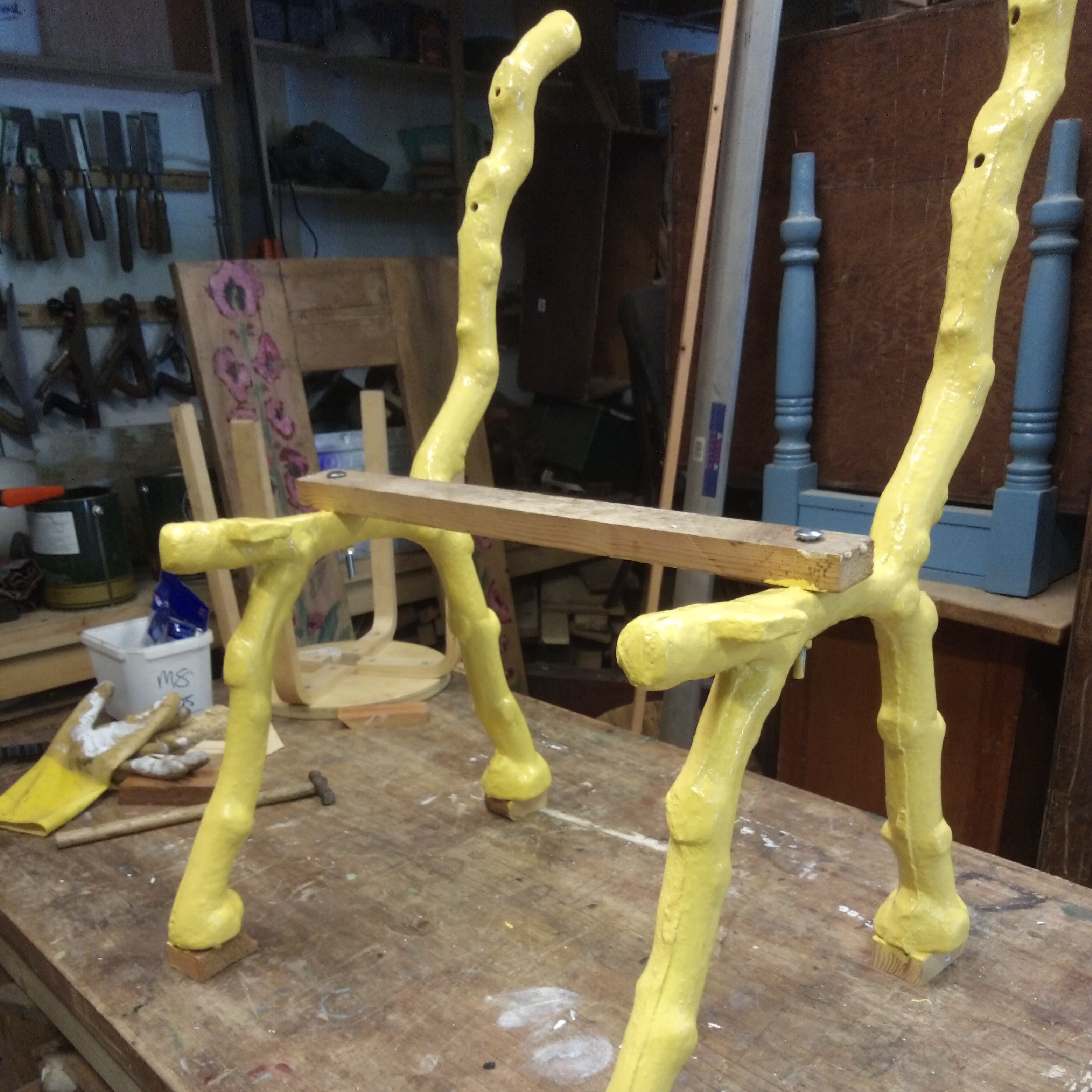 Yellow metal chair frame on a workshop table with tools and materials in the background