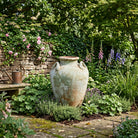 Decorative garden with a large stone vase, flowers, and a stone wall.